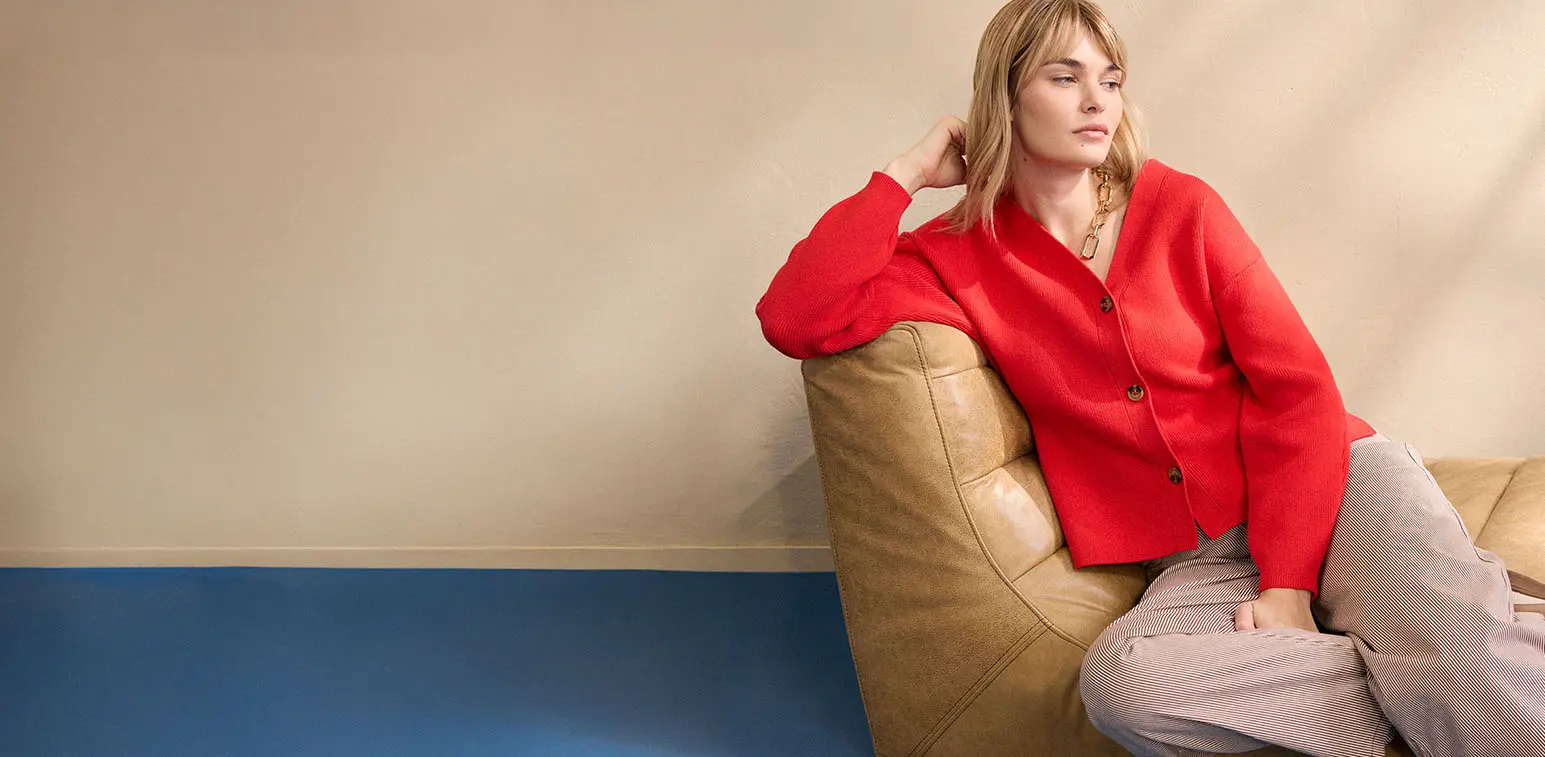 De vrouw draagt een rode cardigan met beige broek.