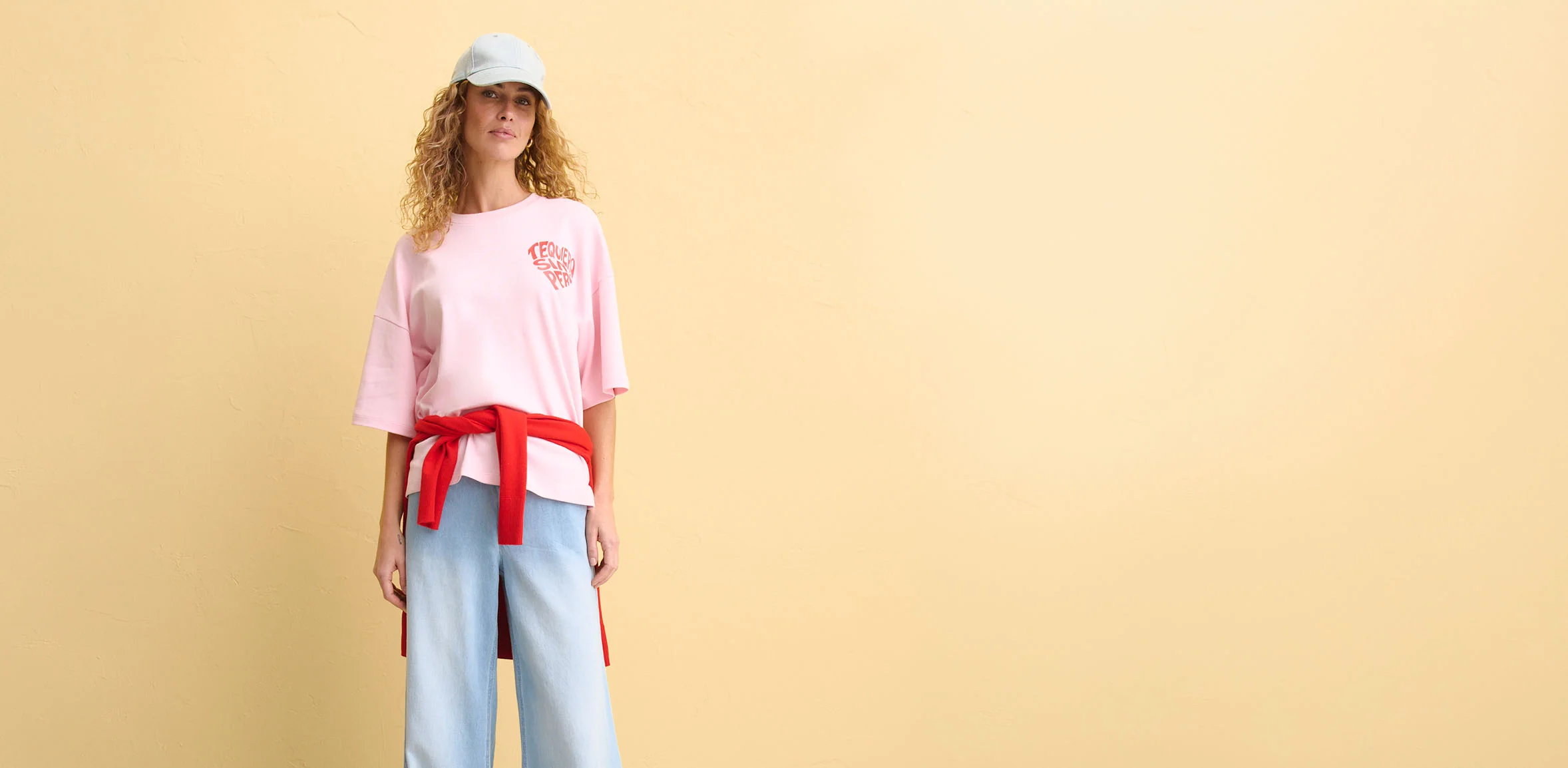 Roze oversized T-shirt met logo, lichtblauwe flared broek en rode riem.