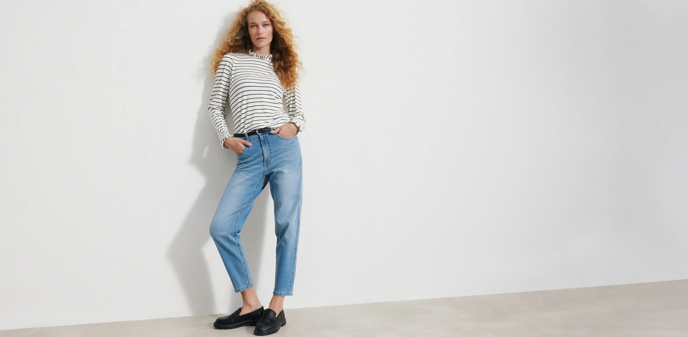 "Lichtblauwe mom‑jeans met een hoge taille en licht taps toelopende pijpen, gemaakt van zacht, gewassen denim, gecombineerd met een donkerblauwe geribde top en bruine loafers."
