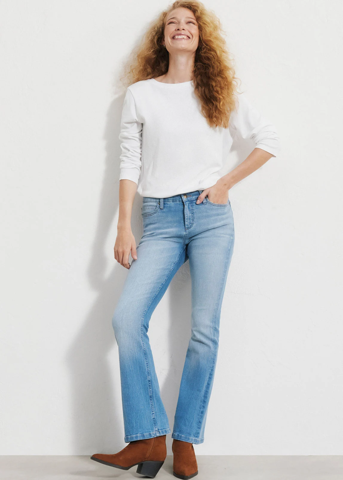 "Donkerblauwe flared‑jeans, nauw aansluitend op de bovenbenen en uitlopend naar beneden, gemaakt van glad, licht verweerd denim, gecombineerd met een witte longsleeve en bruine schoenen."