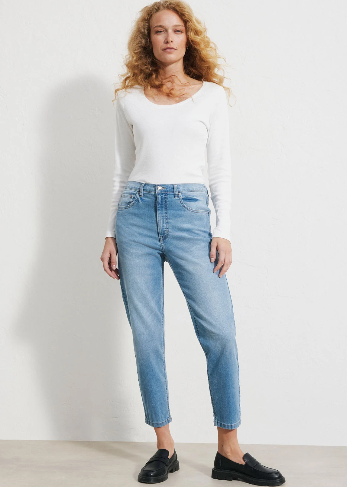 "Lichtblauwe mom‑fit jeans met een hoge taille en licht toelopende pijpen, gemaakt van zacht, verweerd denim, gecombineerd met een wit T‑shirt en bruine schoenen."