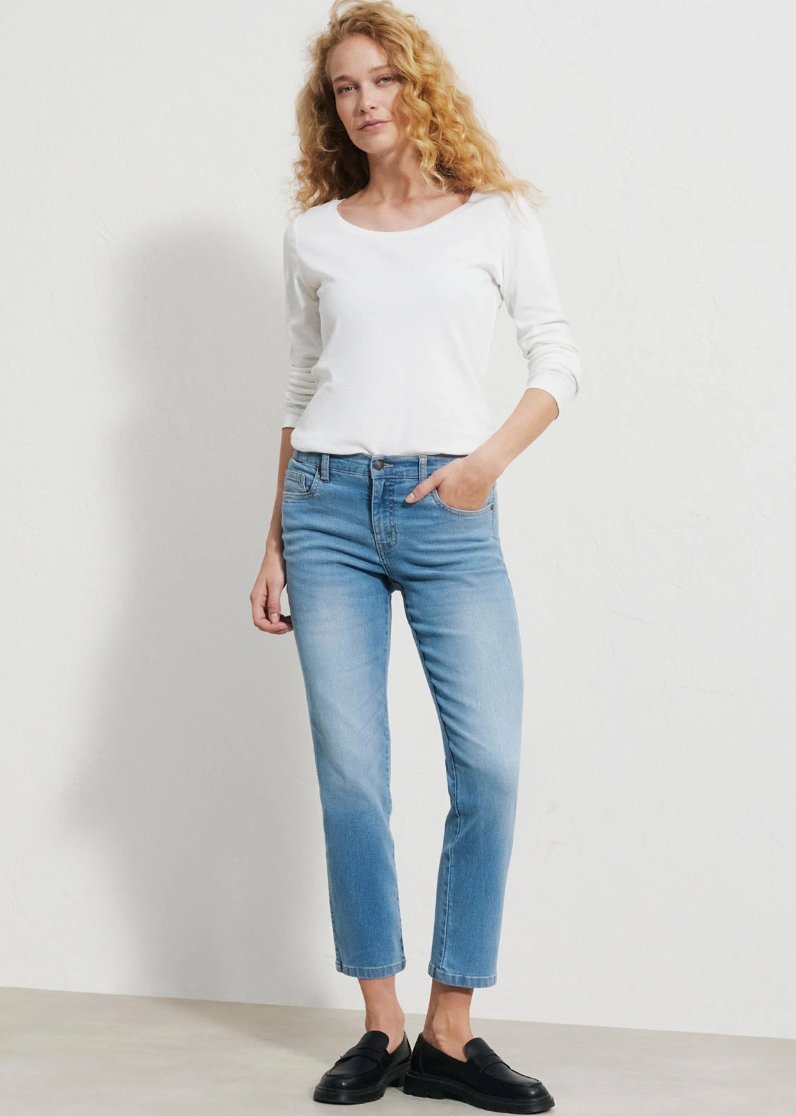 Blauwe jeans met een rechte snit (straight fit), met een hoge taille en subtiele slijtage-accenten, gecombineerd met een wit T‑shirt en bruine schoenen met een lage hak.