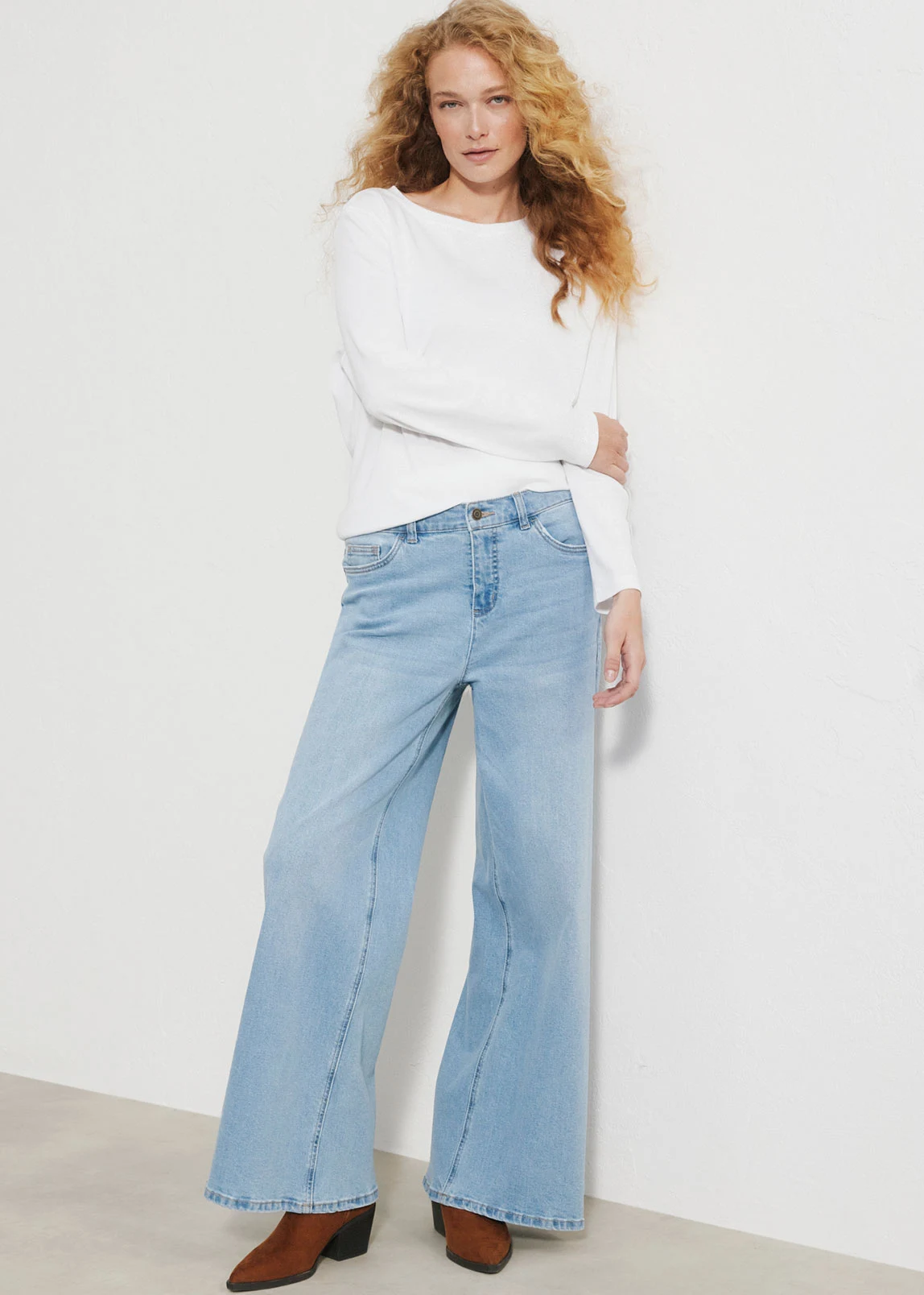 "Donkerblauwe wide‑leg jeans met een hoge taille en een gladde, egale denimstructuur, gecombineerd met een witte longsleeve en witte sneakers."