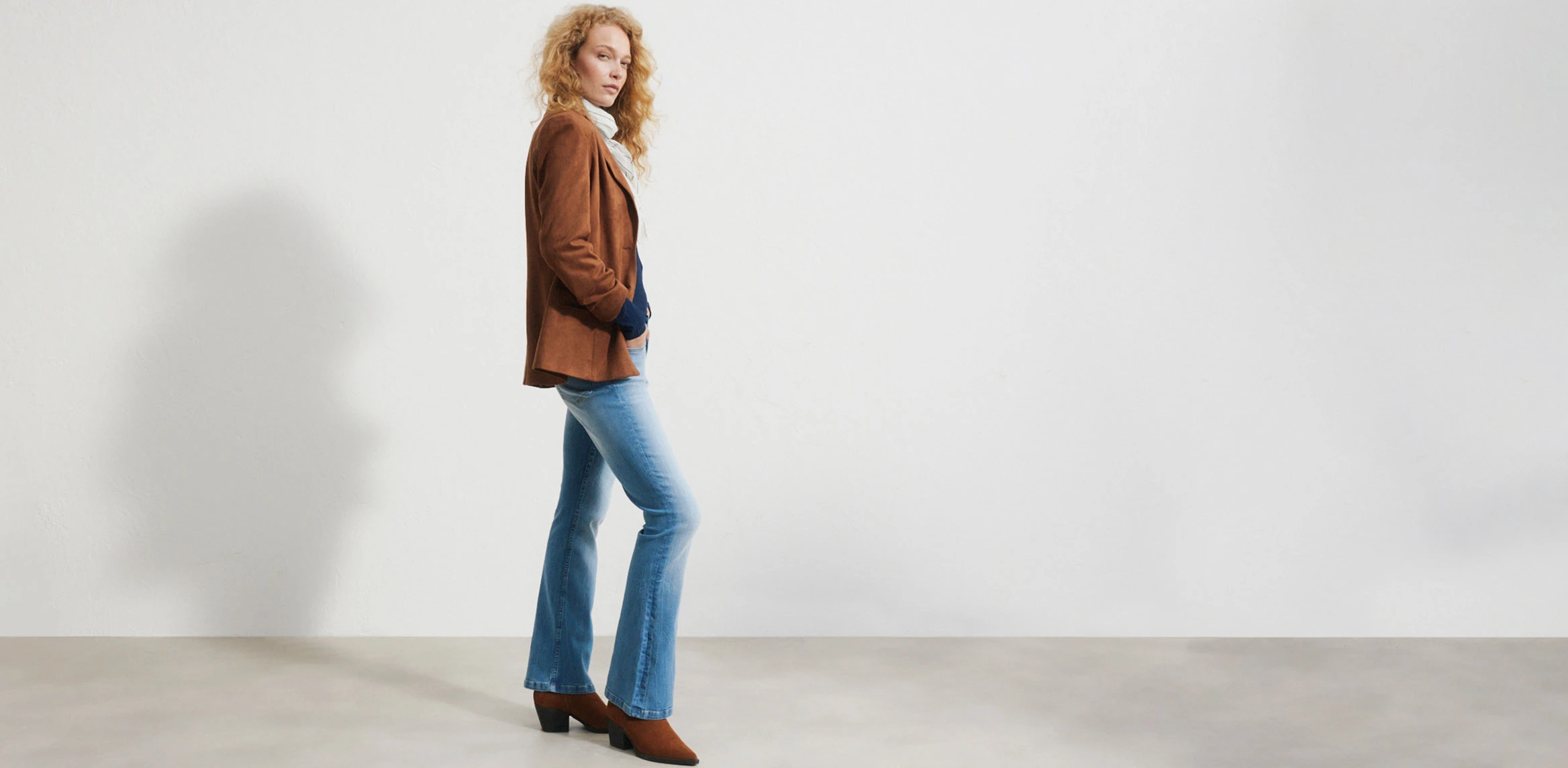 "Donkerblauwe flared‑jeans, nauw aansluitend op de bovenbenen en wijder uitlopend vanaf de knie, gemaakt van glad, licht verweerd denim, gecombineerd met een wit T‑shirt, een bordeauxrode jas en bruine schoenen."