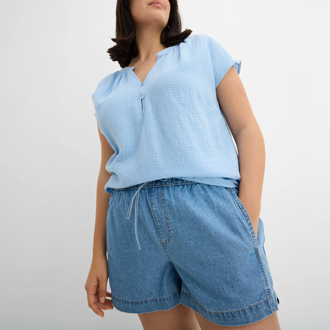 Lichtblauw mouwloos shirt met ritssluiting en losjes vallende spijker short als relaxte zomerlook.